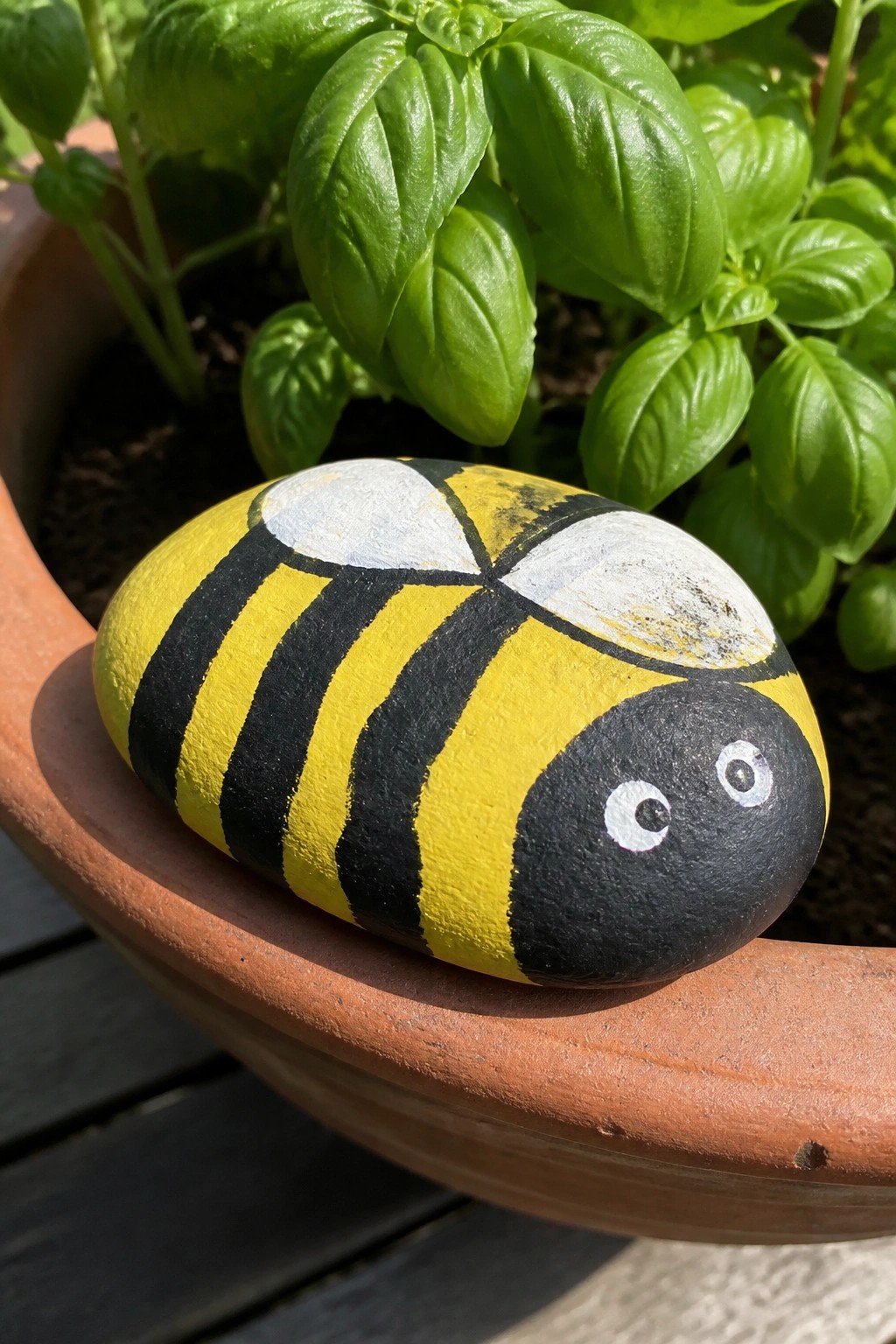Painted rock bee with yellow-black stripes and white eyes on terracotta pot rim