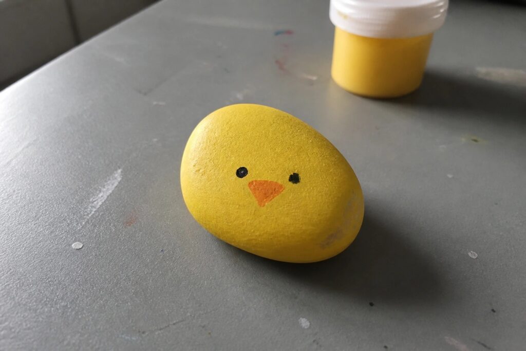 24 Fun Rock Painting Ideas for Kids Using Simple Colorful Designs Yellow painted rock with chick face, black eyes, and orange beak