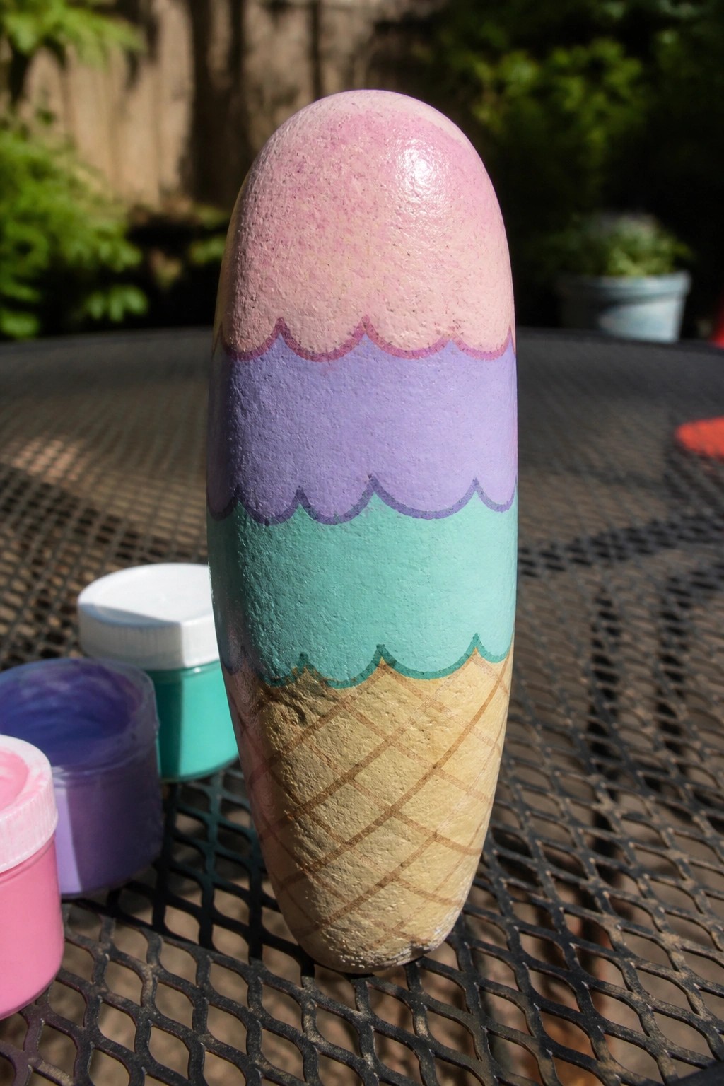 Painted rock ice cream cone with pink, purple, and teal scoops on mesh table