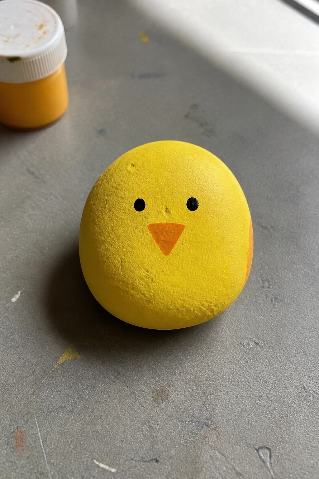 Yellow painted rock with chick face, black eyes, and orange beak
