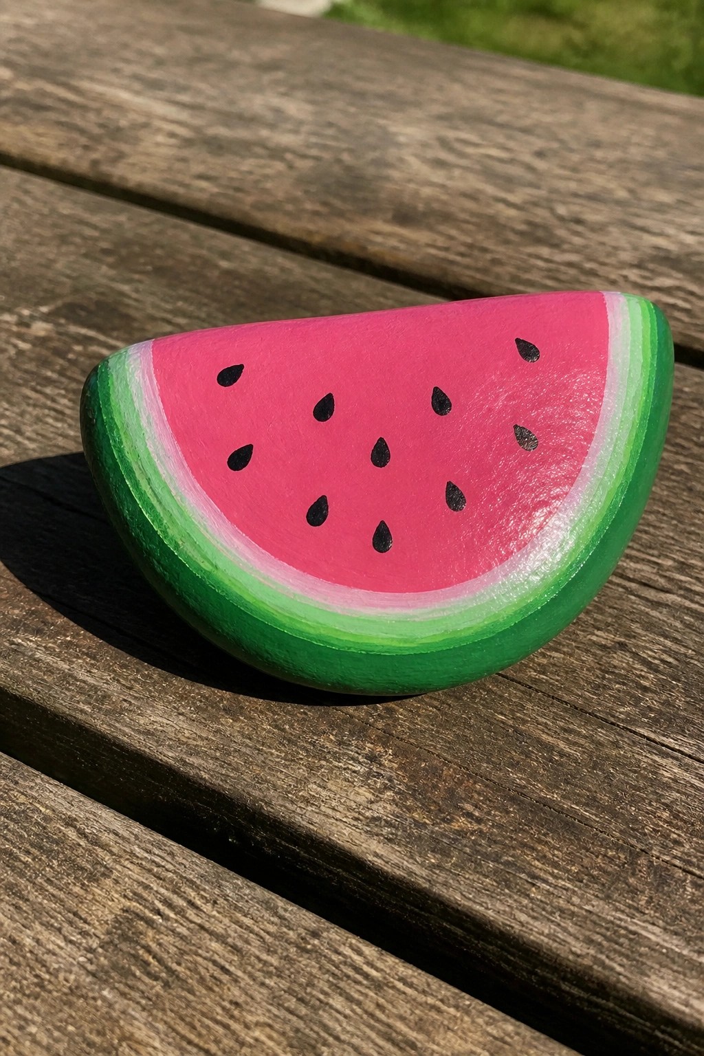Painted rock shaped like watermelon slice with pink flesh and green rind on wood