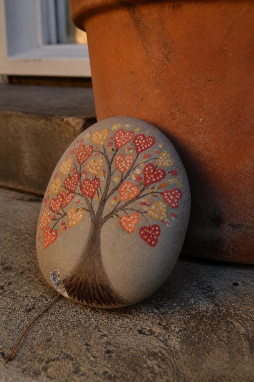 Painted stone with tree of red, orange, yellow heart leaves beside terracotta pot