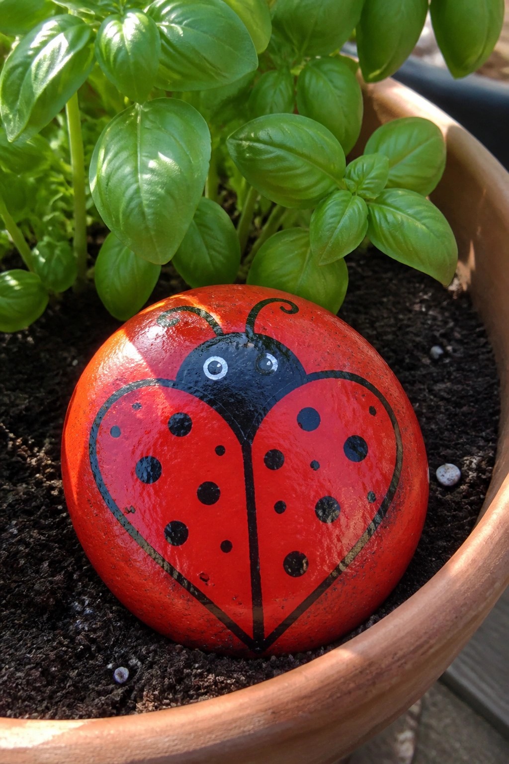 Painted red ladybug rock with black spots in potted plant soil.