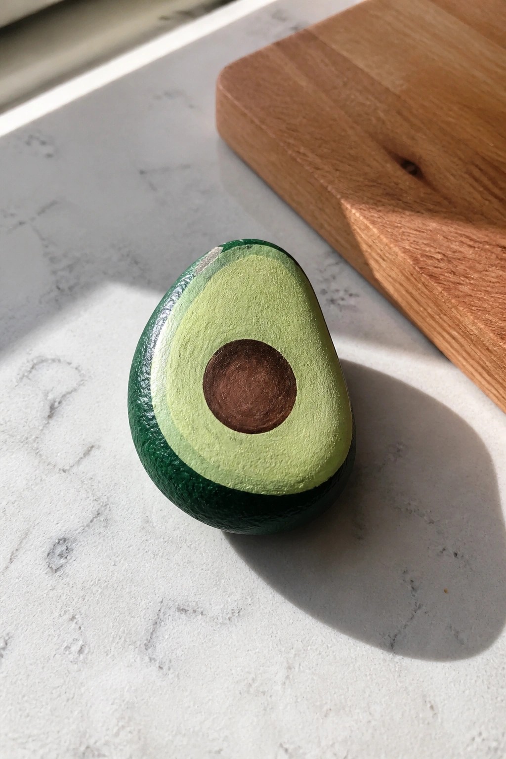 Painted wooden avocado half on marble countertop beside wooden cutting board