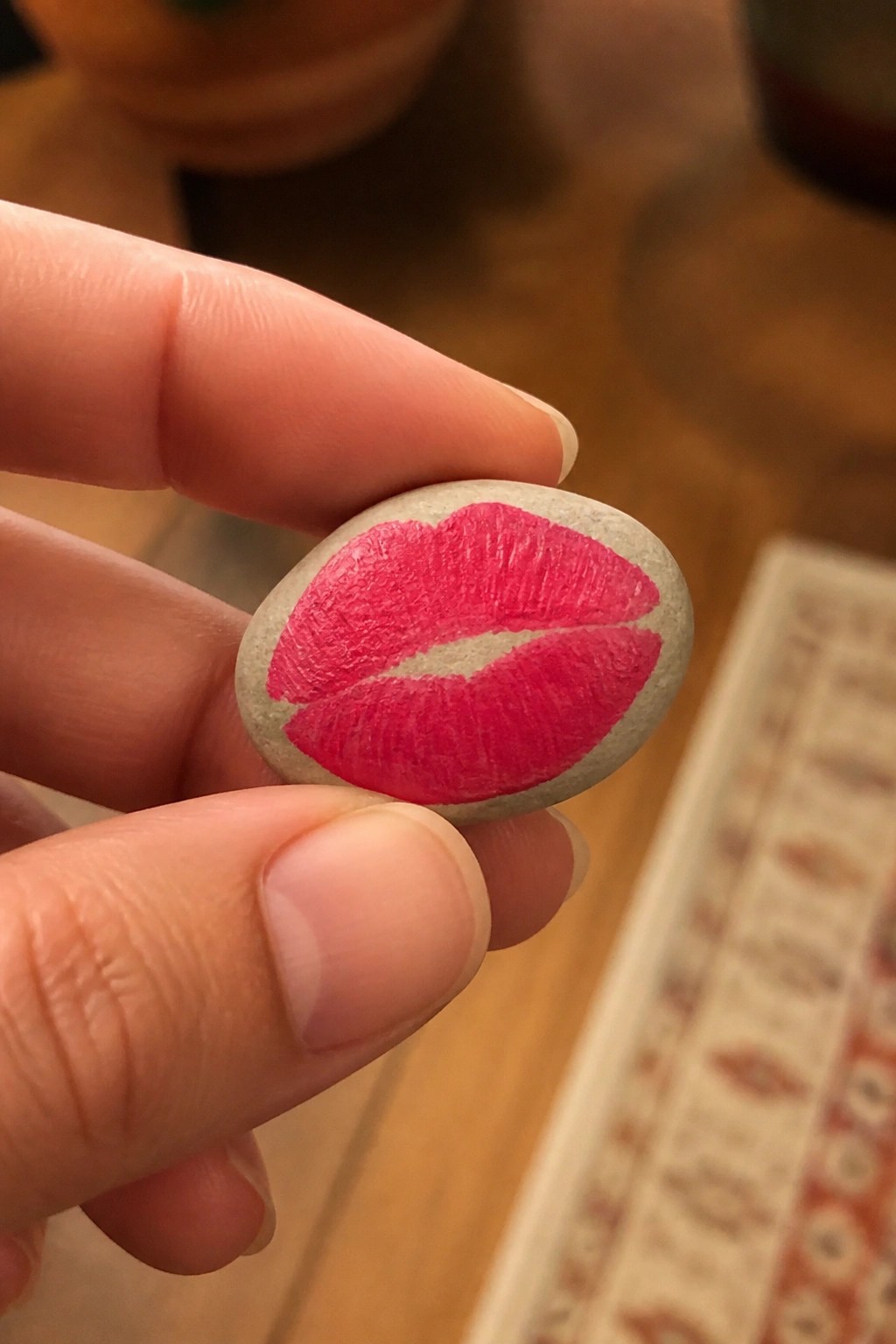 Hand holding small gray stone painted with vibrant pink lips