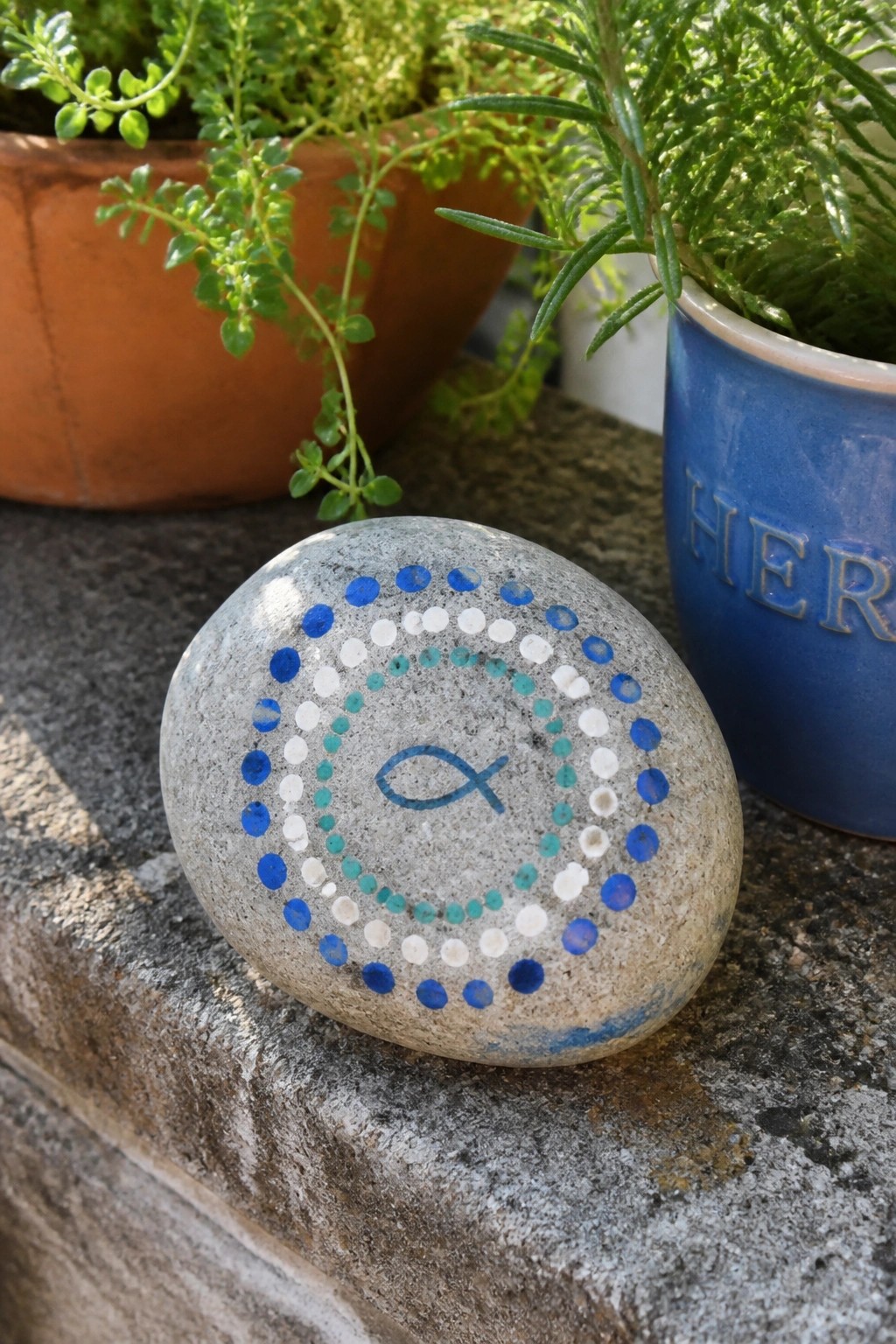 Gray stone with blue fish symbol encircled by rings of blue white teal dots near plants