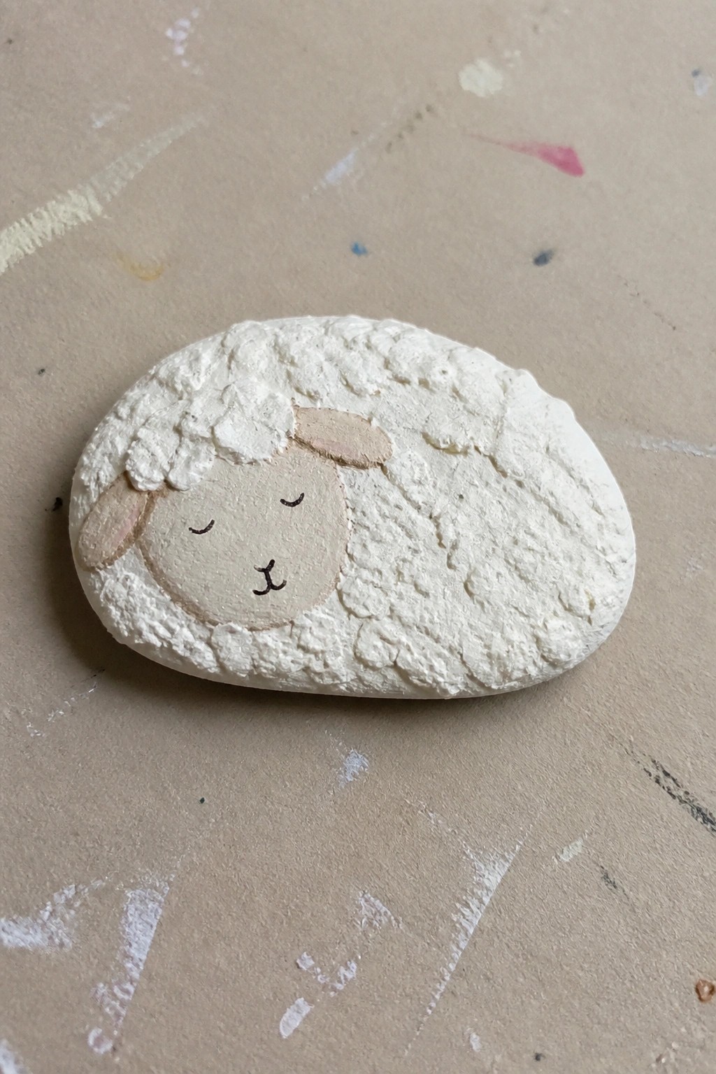 Painted white rock shaped like sleeping sheep with textured wool and beige face