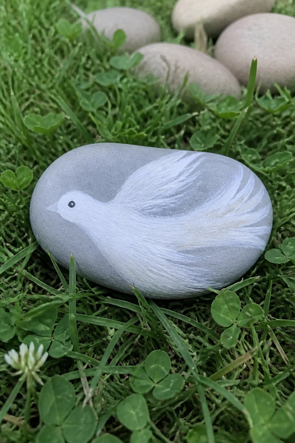 Gray stone painted with white bird on green grass with clover