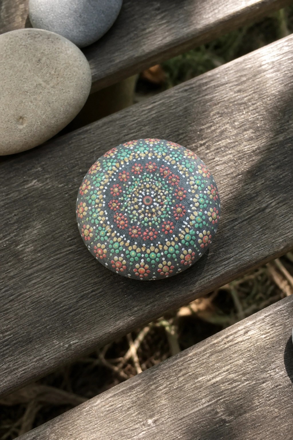 Colorful mandala stone with red green yellow dots on wooden surface