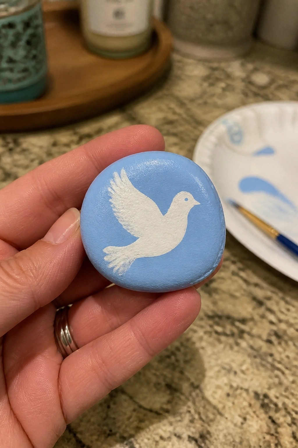 Hand holding light blue painted rock with white dove silhouette on counter