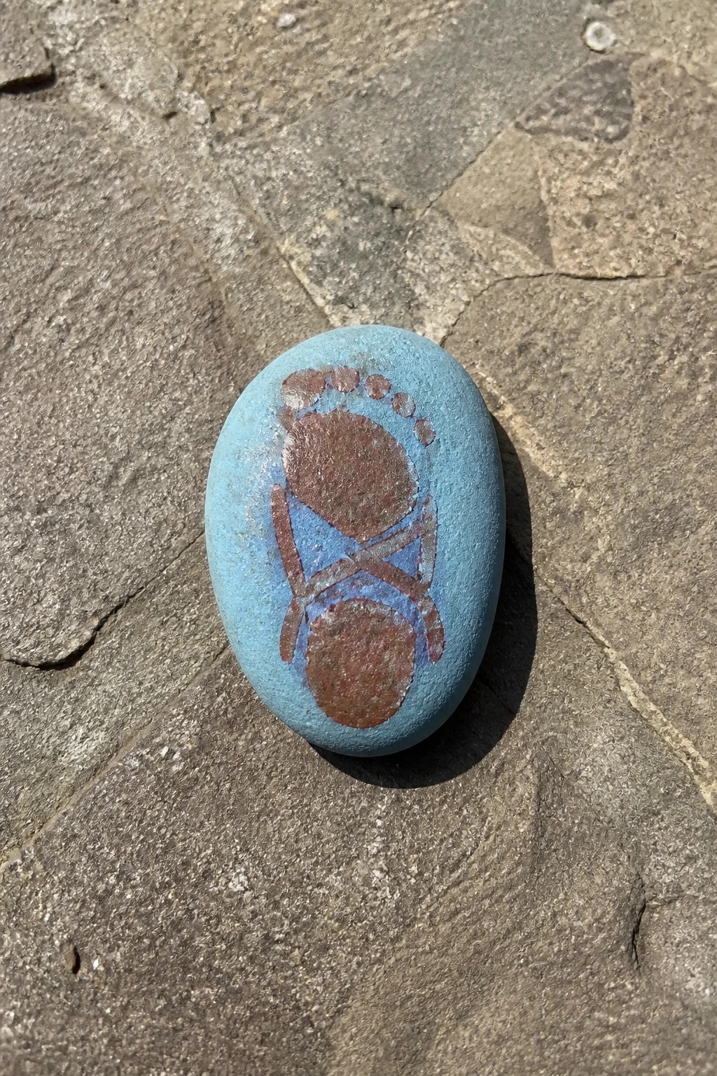 Blue oval stone with brown footprint design on gray pavement