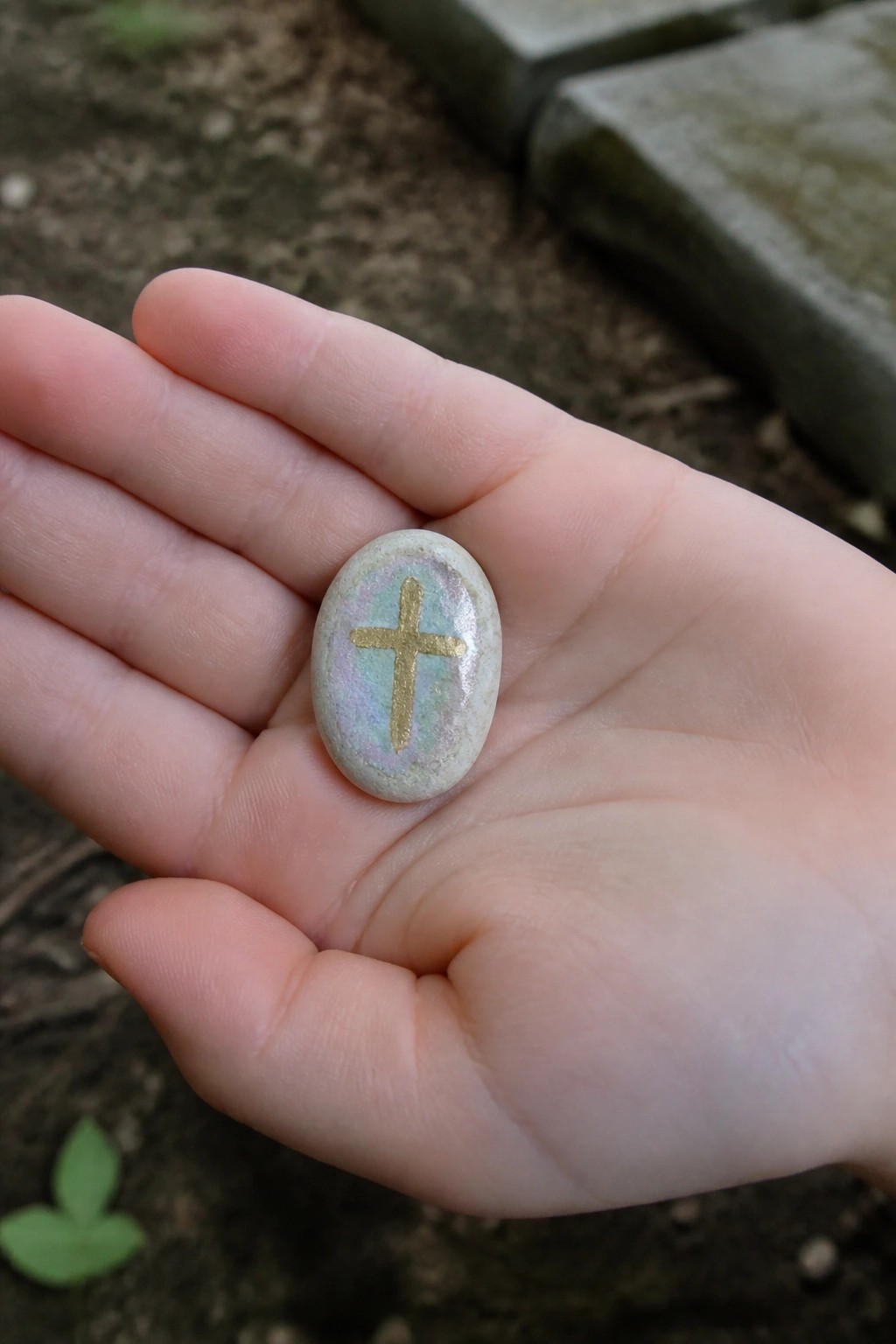 Hand holding iridescent oval stone with gold cross symbol