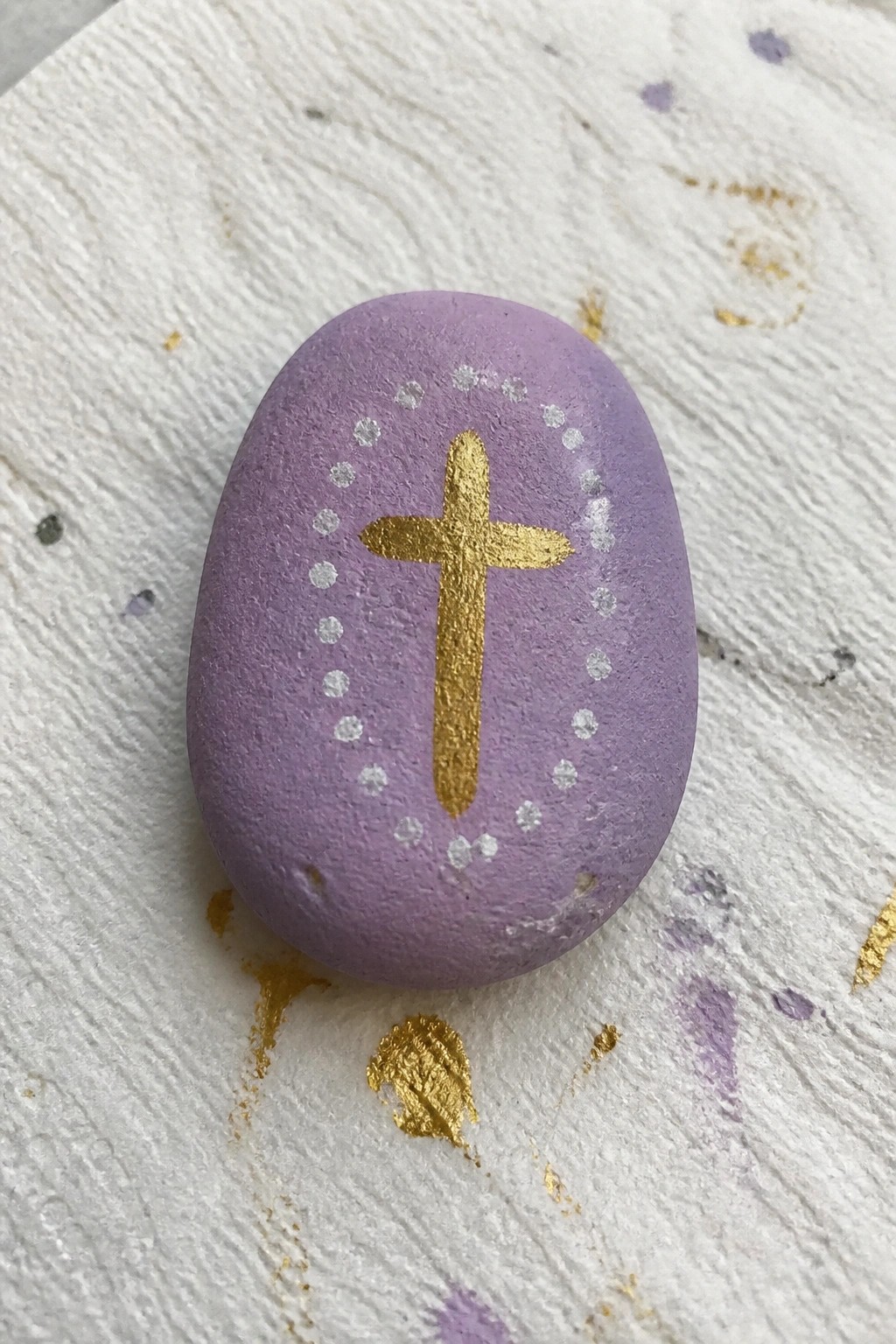 Purple stone with gold cross and white dotted circle on textured surface.