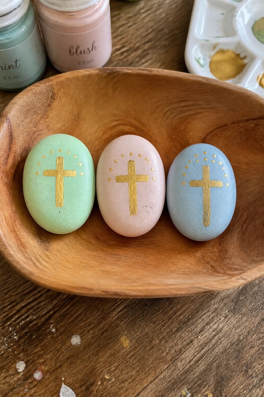 Three pastel rocks with gold crosses and dots in wooden bowl