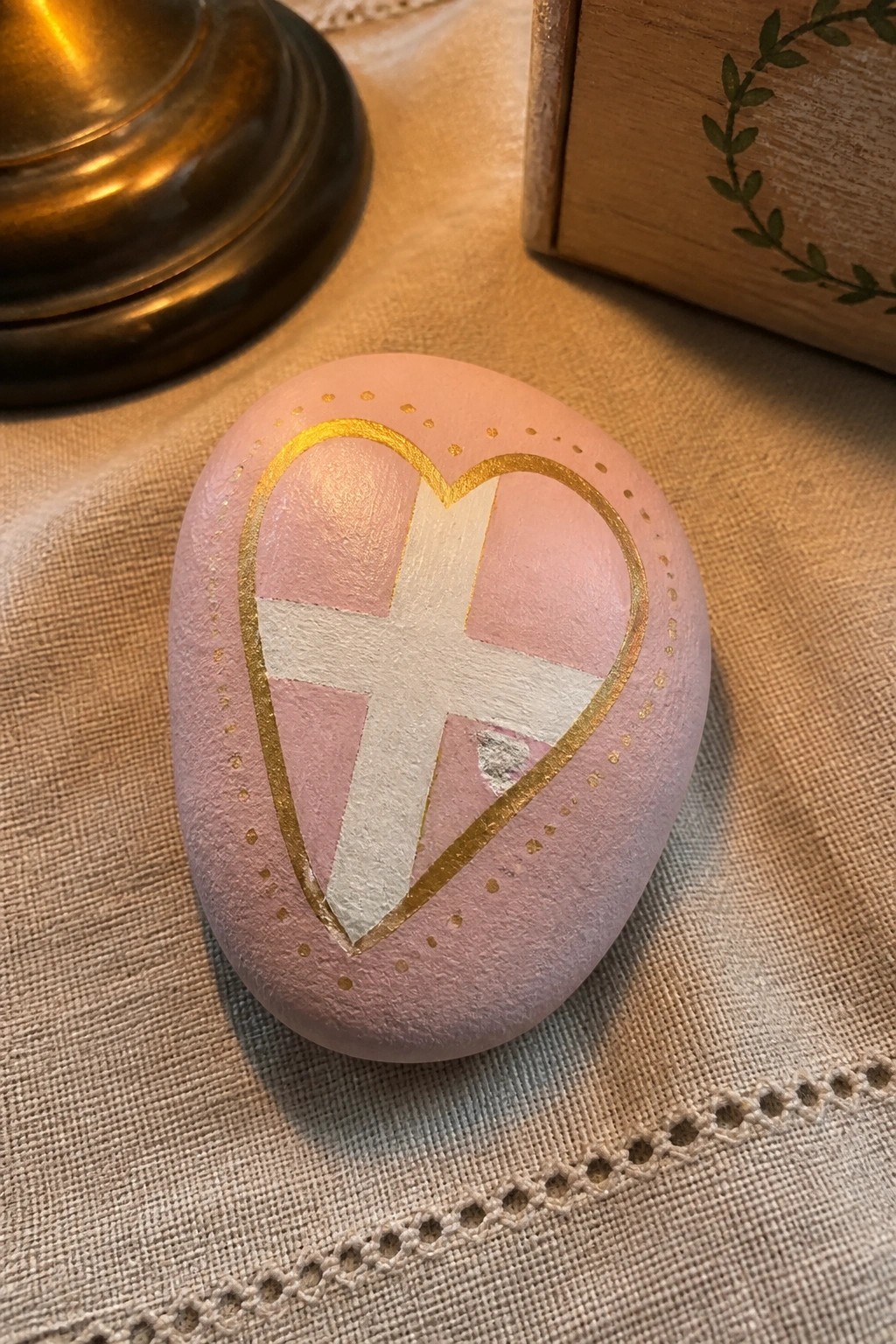 Pink stone with gold heart outline and white cross on beige fabric
