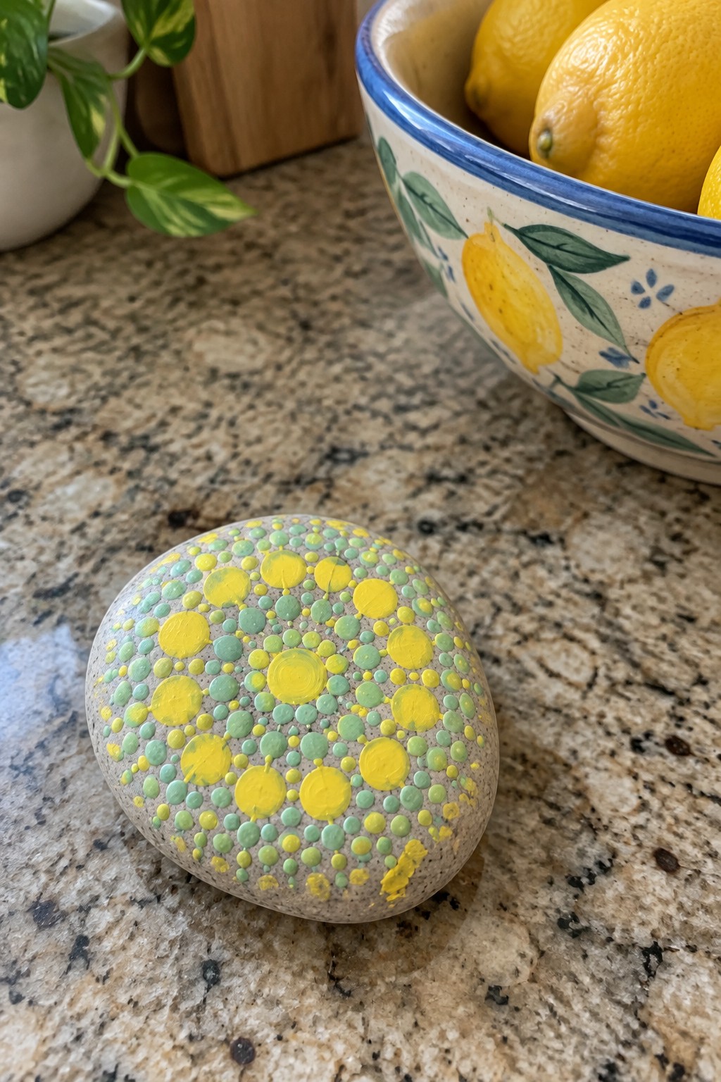 Painted gray rock with yellow and green dots on granite counter near lemon bowl
