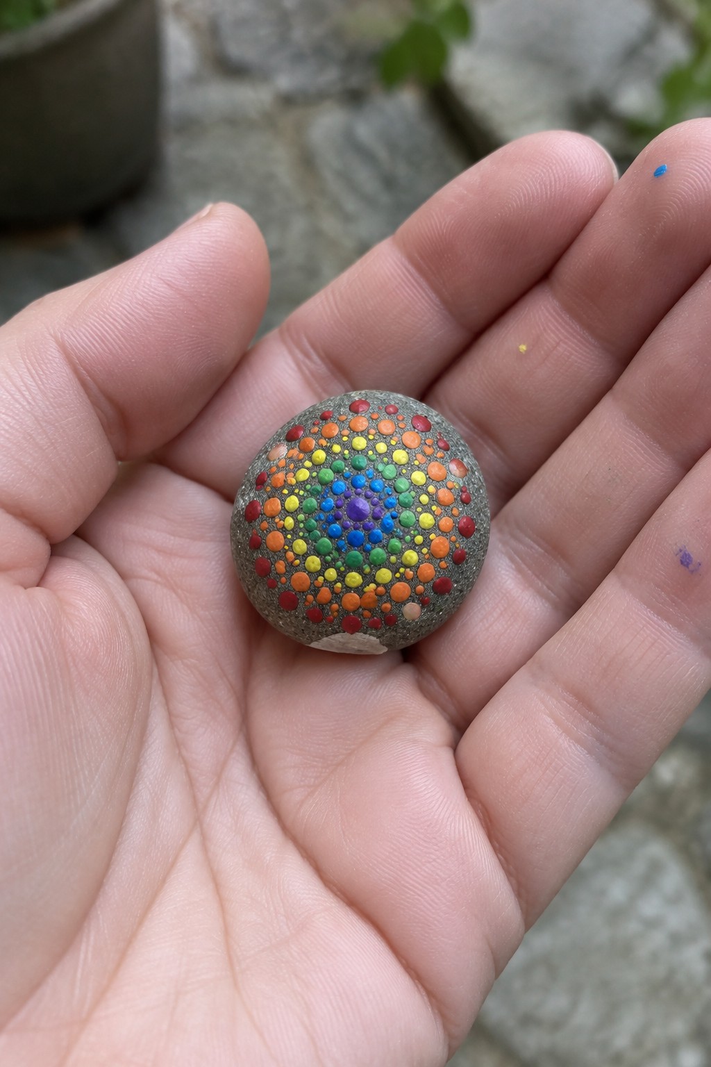 Hand holding small stone painted with rainbow concentric dot mandala
