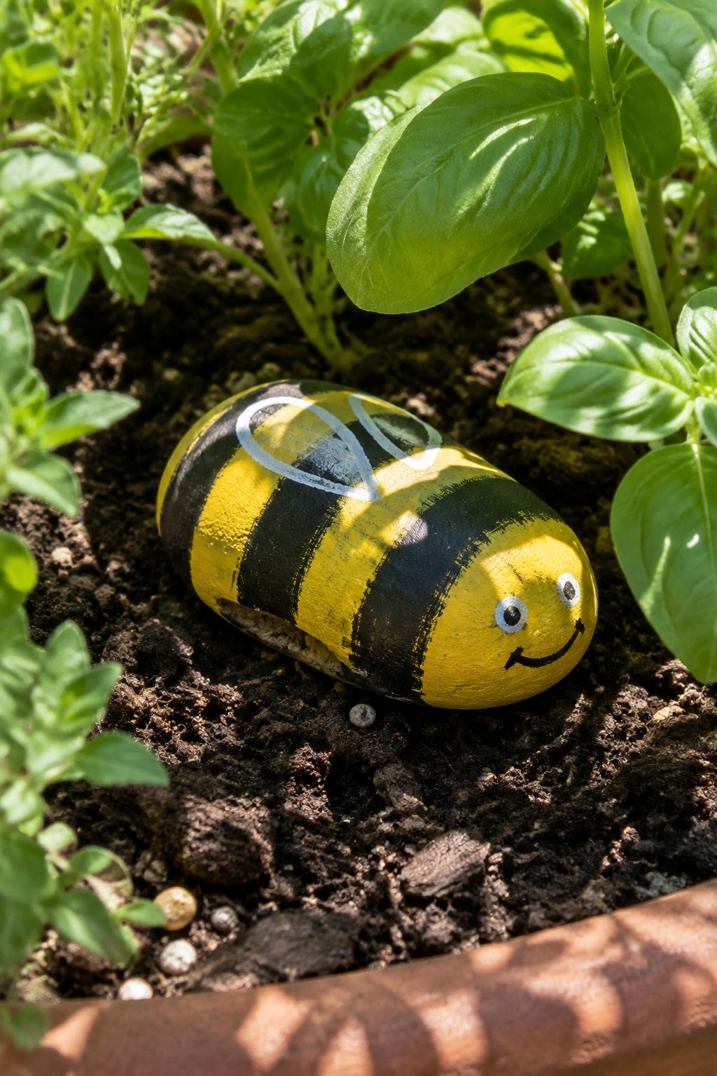 Yellow and black striped painted rock bee with smiling face in garden soil