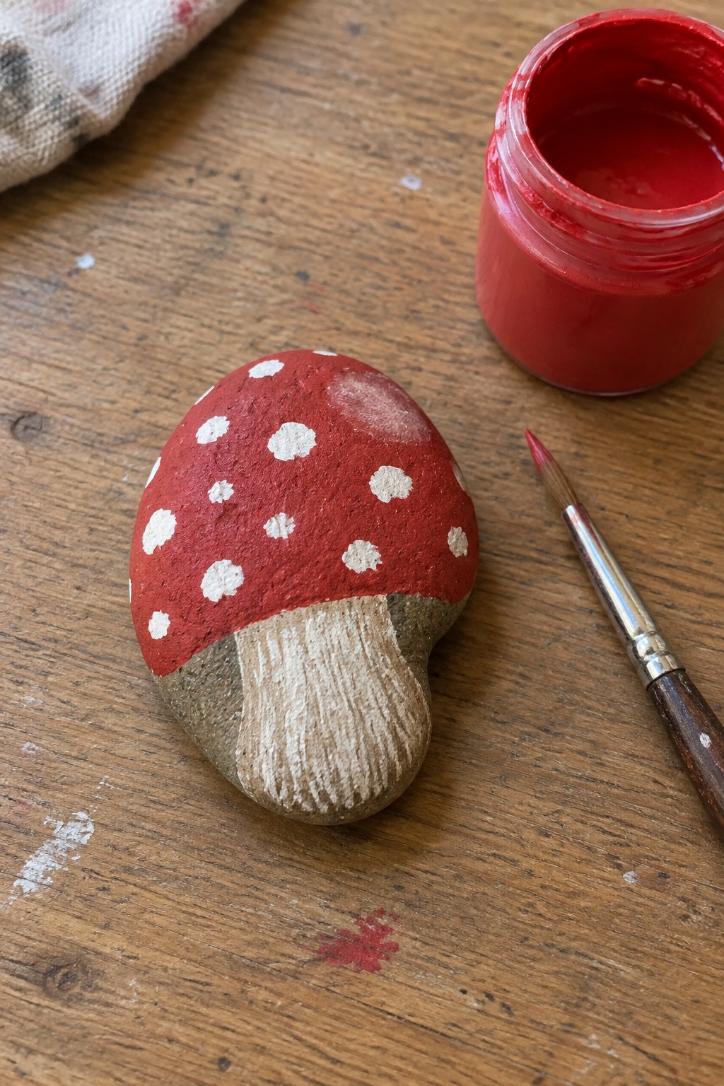 Red stone mushroom with white dots beside red paint jar and brush on wood