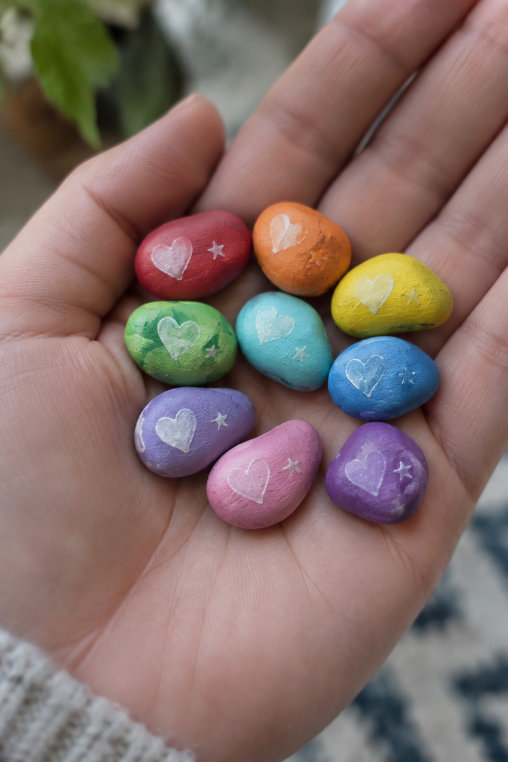 Open hand holding rainbow rocks painted with white hearts and stars.