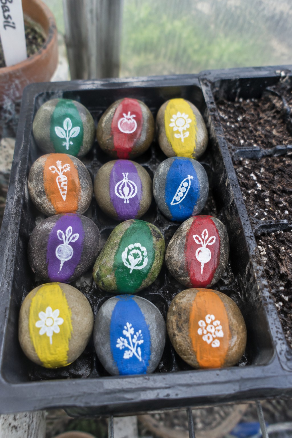 Painted rocks with vegetable icons in green, red, yellow, and blue arranged in a tray