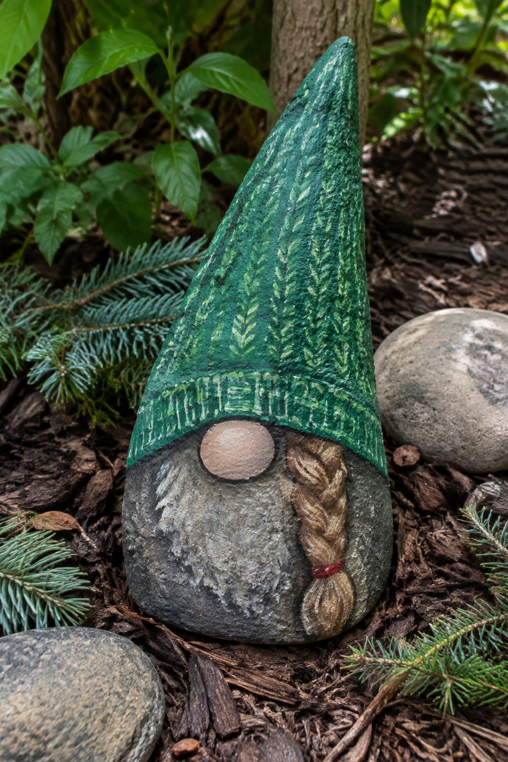 Painted rock gnome with green patterned hat, beige nose, and braided beard.