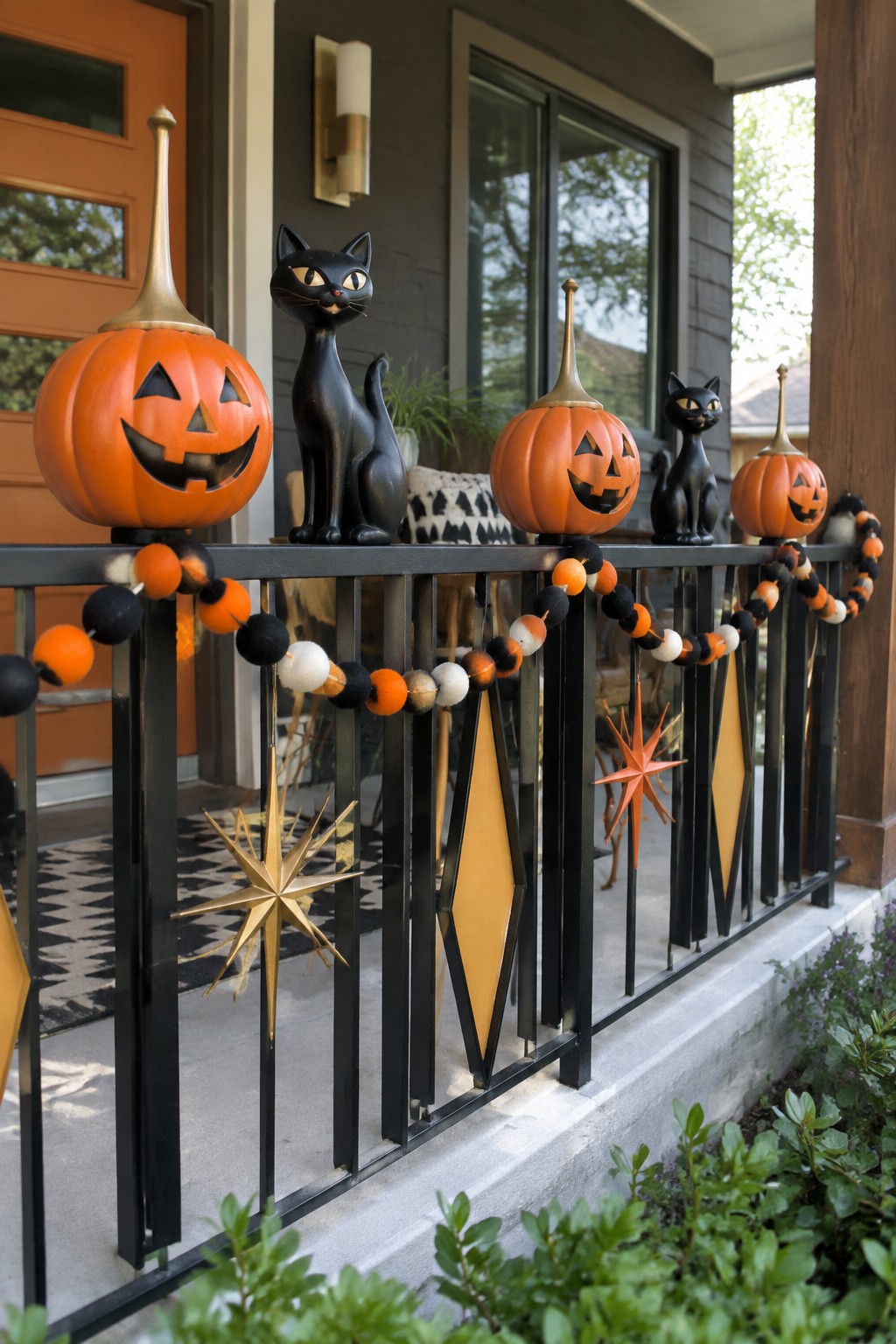 Front porch railing lined with carved orange pumpkins, black cat figurines, and an orange and black felt ball garland.