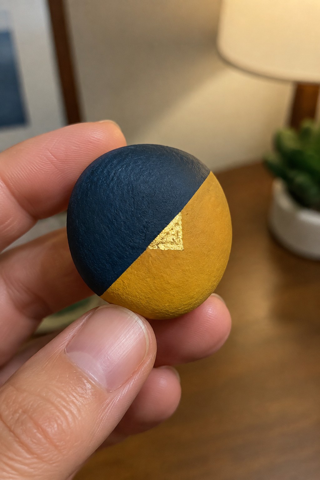 Hand holding small sphere painted navy blue and yellow with gold triangle accent