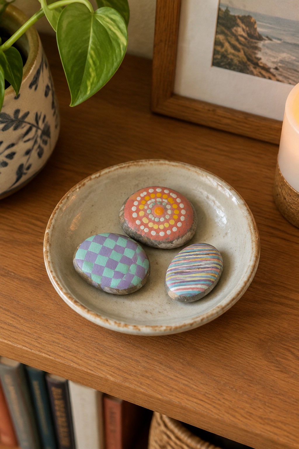 Three painted rocks in a ceramic bowl on a wooden shelf