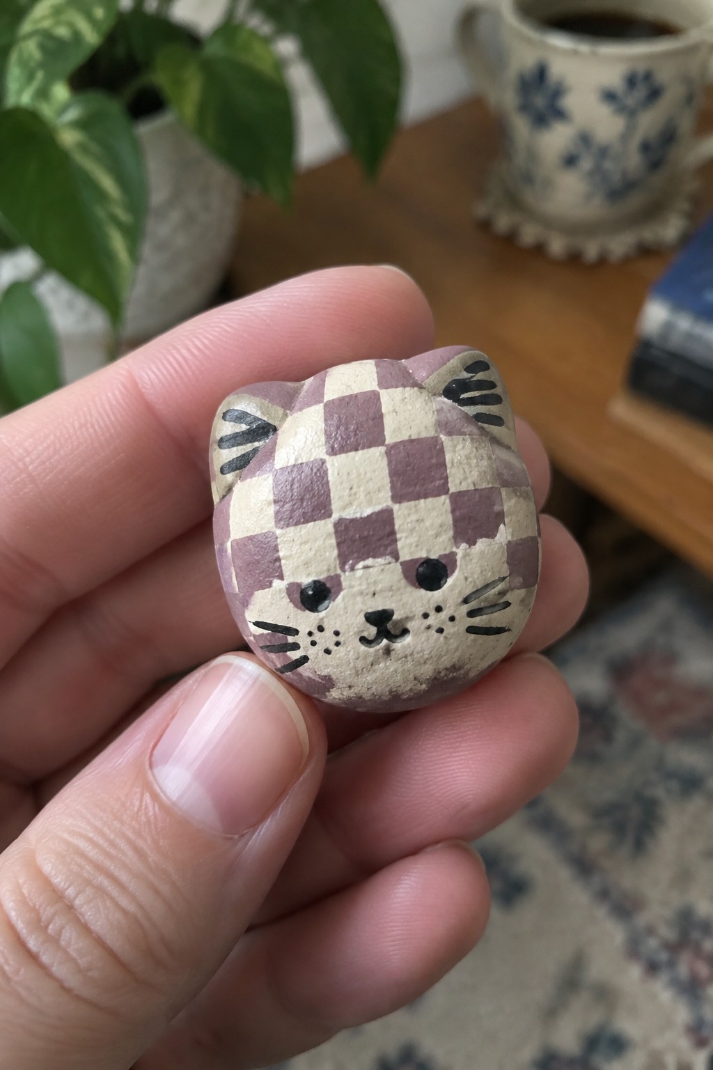 Hand holding small purple-checkered ceramic cat figurine with painted whiskers and eyes