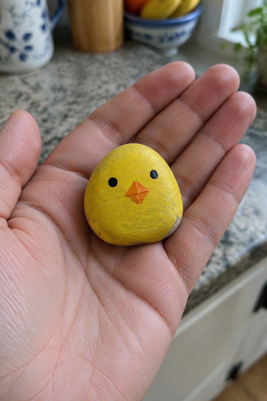 Hand holding yellow painted rock chick with black eyes and orange beak