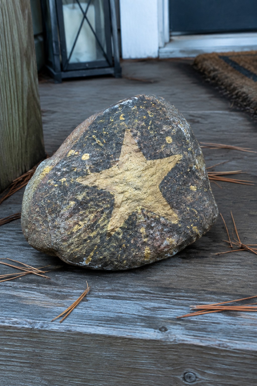 Rock with gold star painted on it, on wooden deck with pine needles