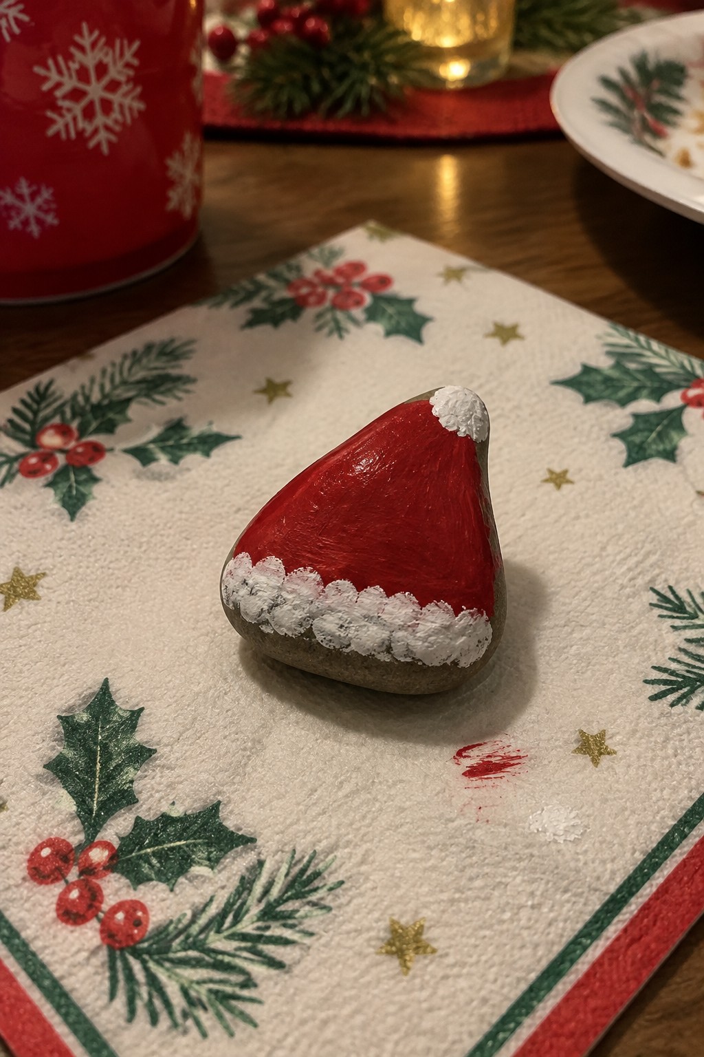 Painted rock as red Santa hat with white trim on holly napkin