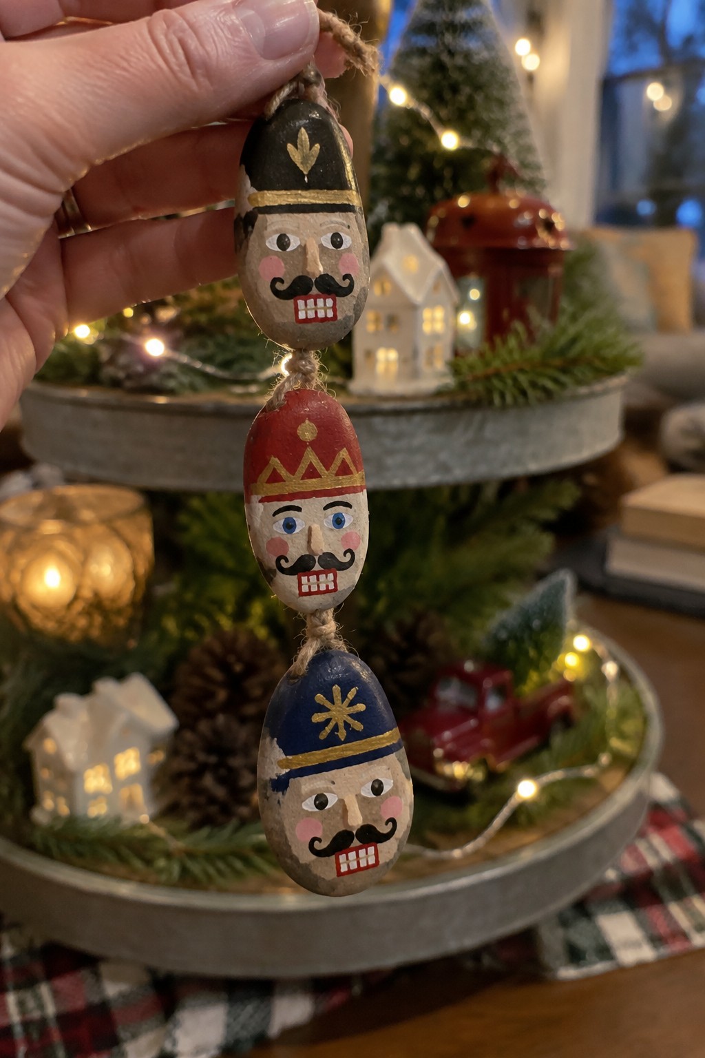 Hand holding three painted stone nutcrackers with black, red, and blue hats on twine.
