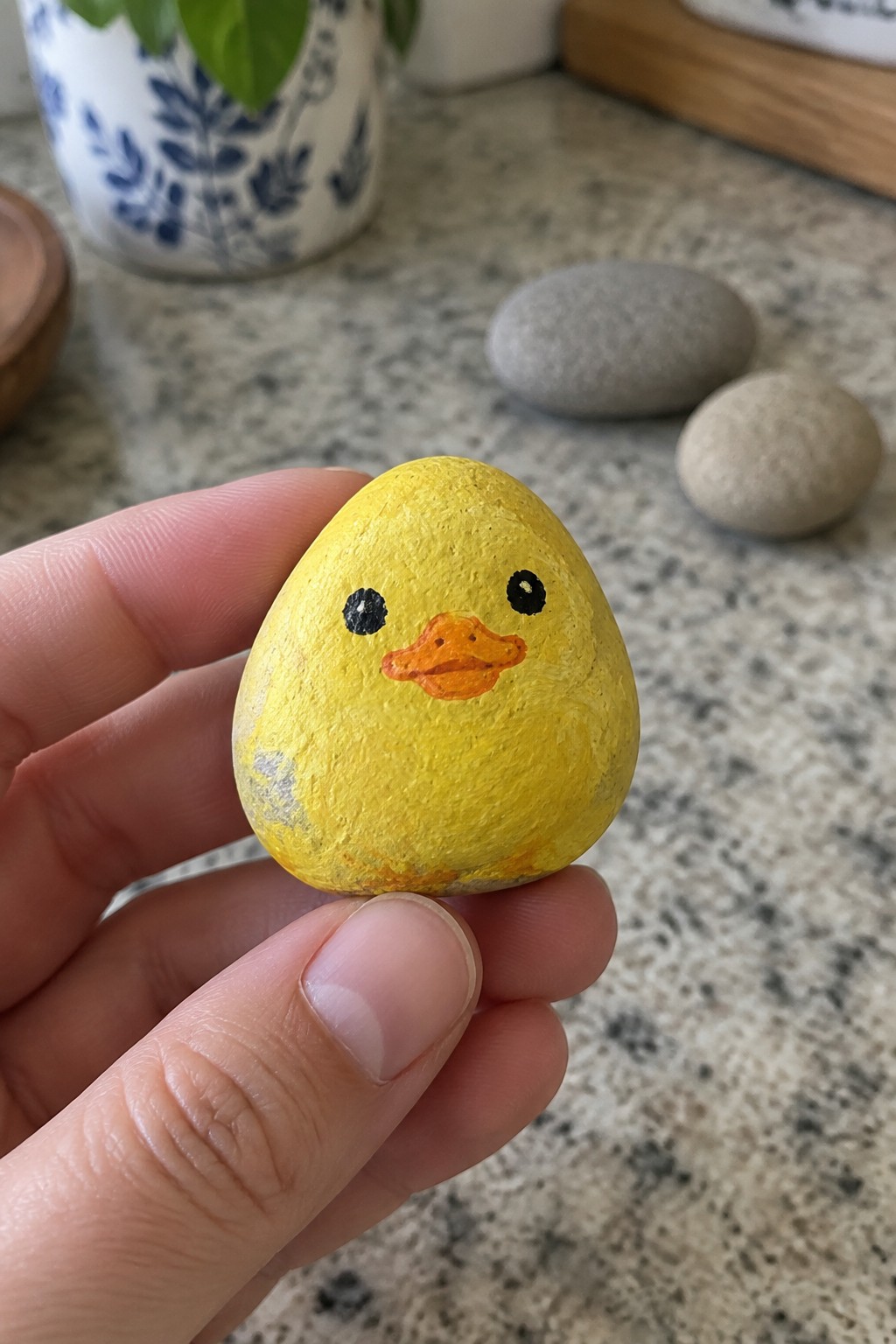Hand holding yellow painted rock duck with orange beak and black eyes