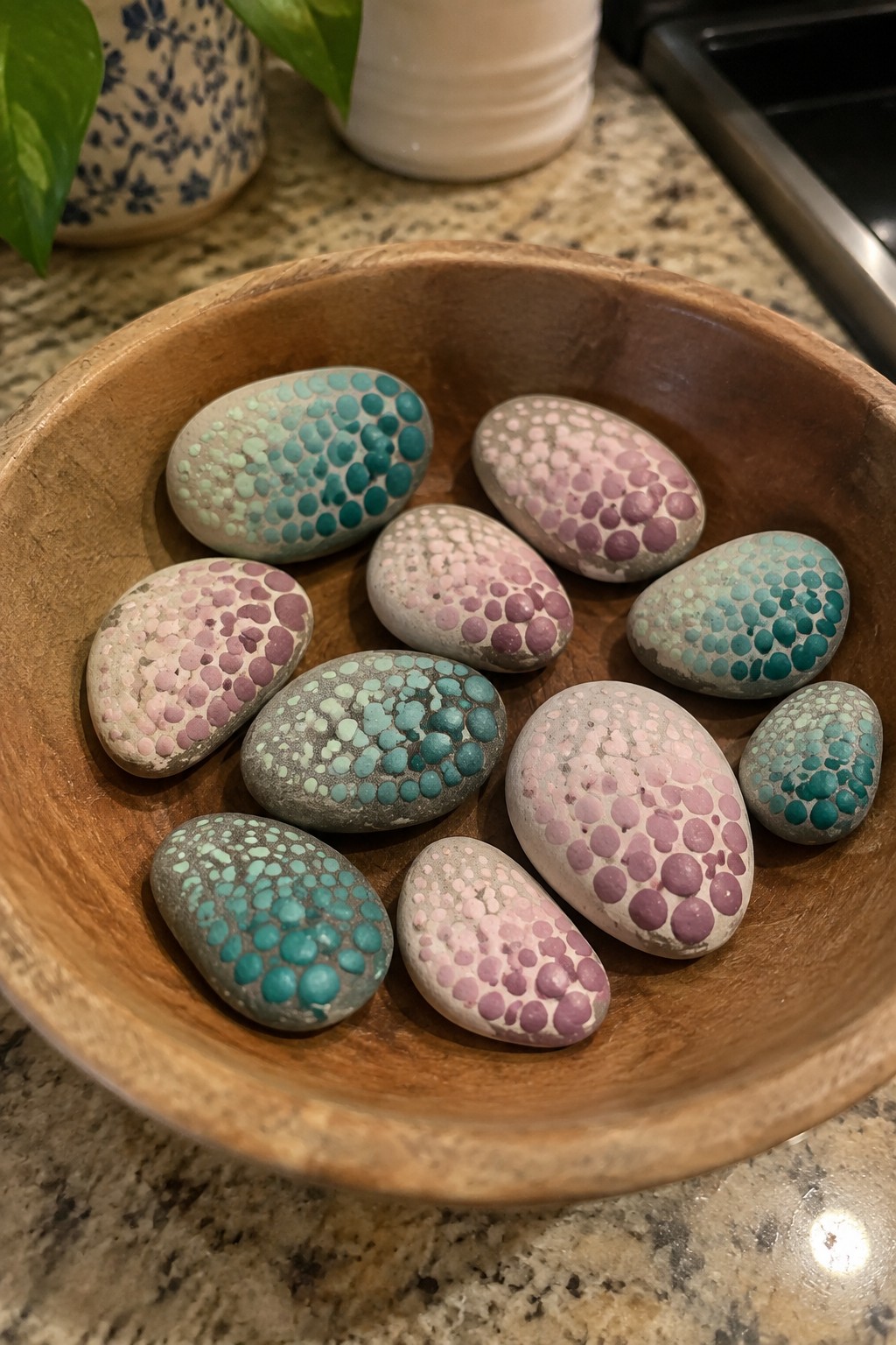 Painted rocks with teal and pink dot patterns filling a rustic wooden bowl.