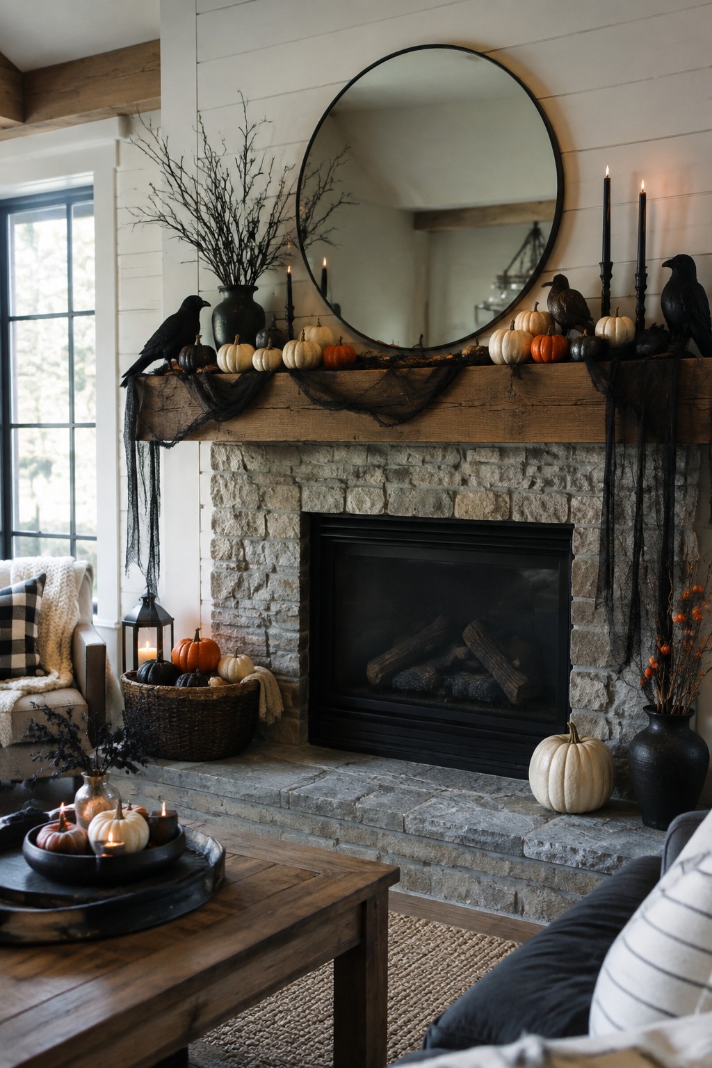 Stone fireplace mantel styled with black bird figures, bare branches in a dark vase, small neutral pumpkins, and black candles for Halloween.