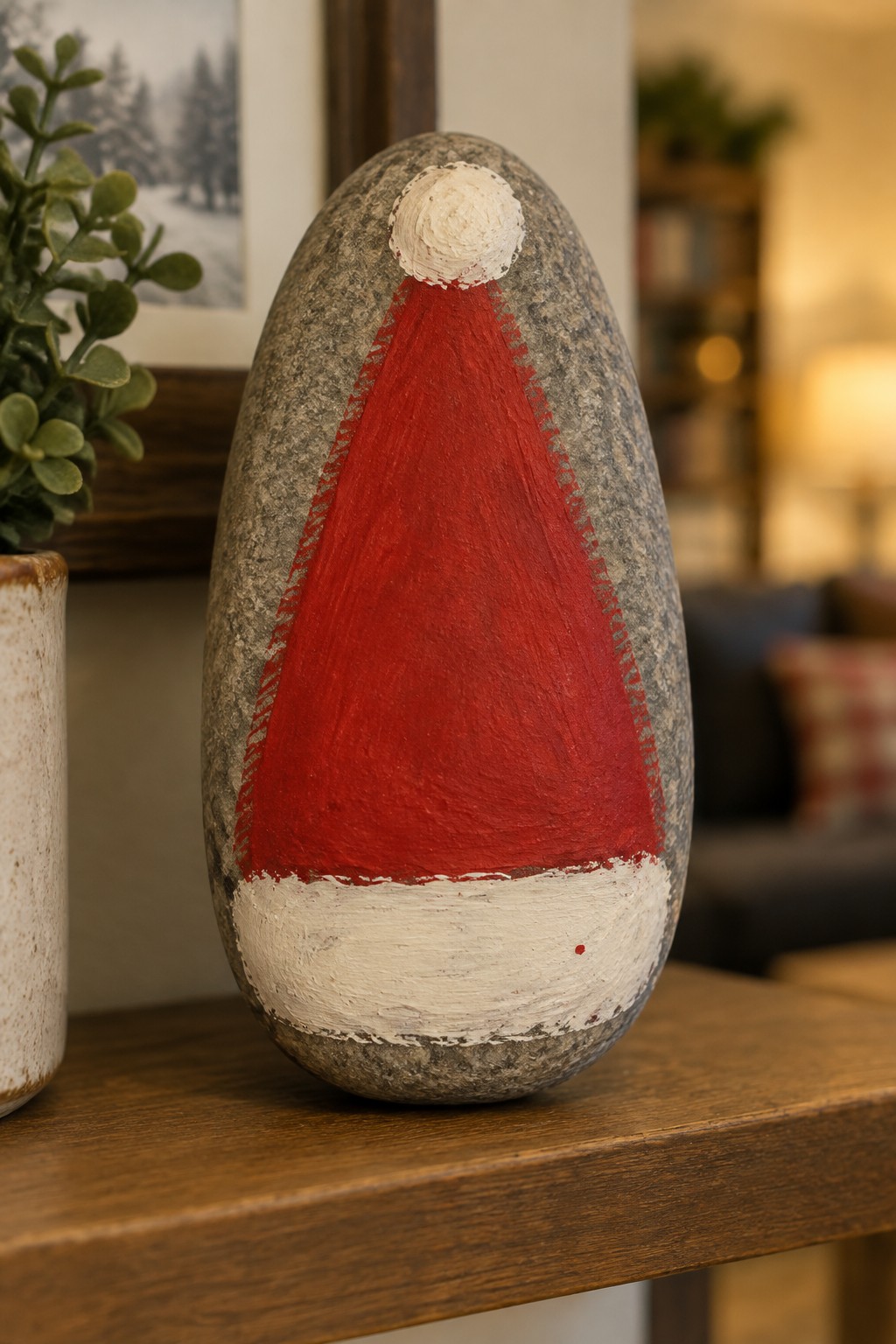 Painted rock with red Santa hat, white brim, and pom-pom on wooden surface
