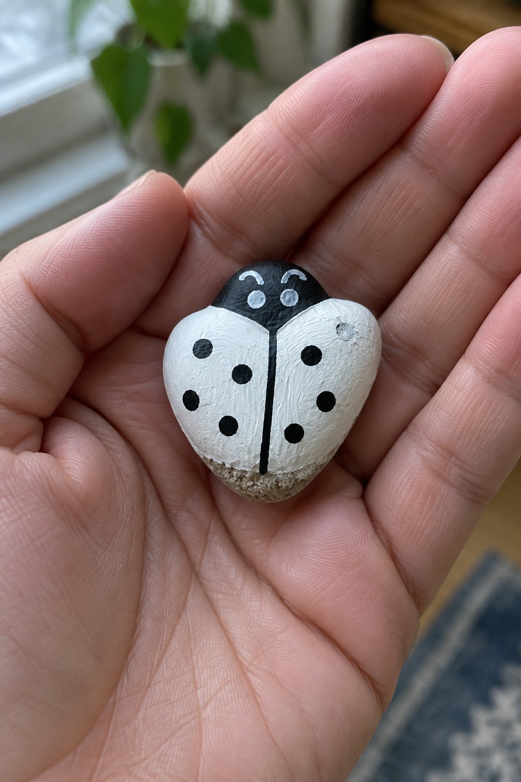 Hand holding a white ladybug rock with black spots and head