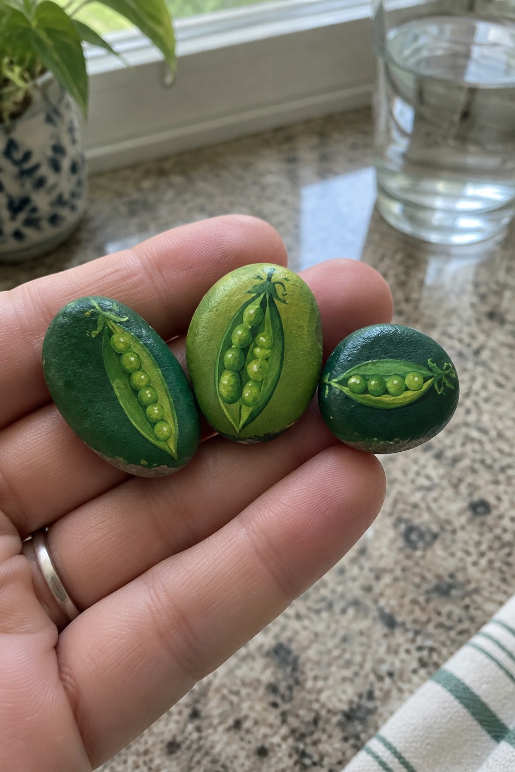 Hand holding three stones painted with green open pea pods.