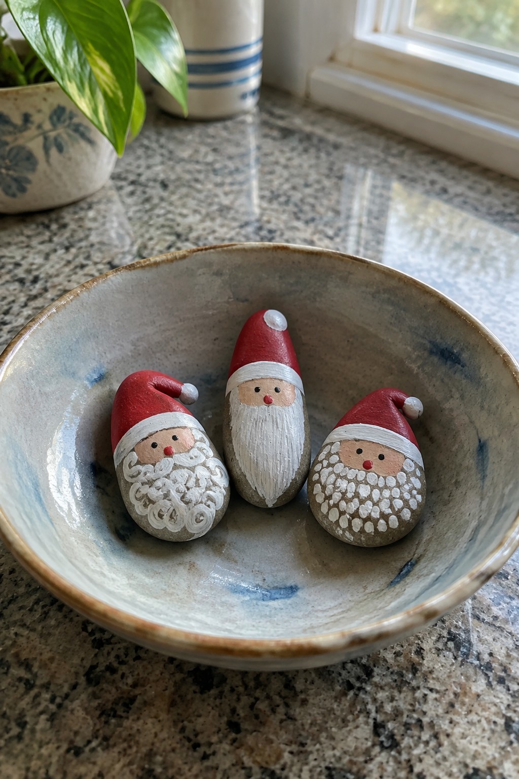 Three painted rock Santas with red hats and beards in a ceramic bowl
