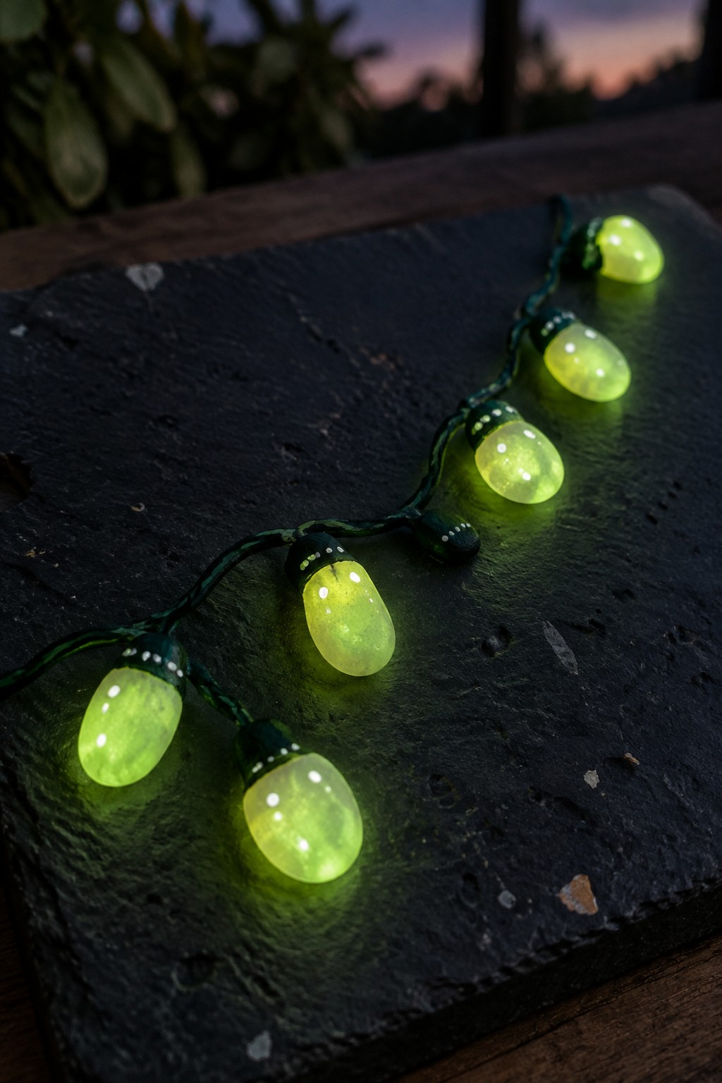 Glowing green string lights on a dark textured slate surface at dusk.
