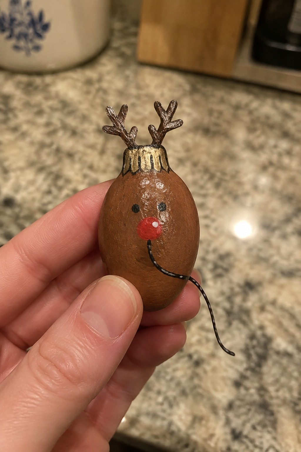 Hand holding small brown painted reindeer with antlers, red nose, and tail