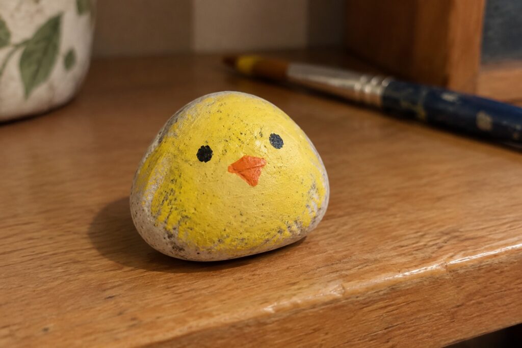 Yellow painted rock chick with black eyes and orange beak on wooden table
