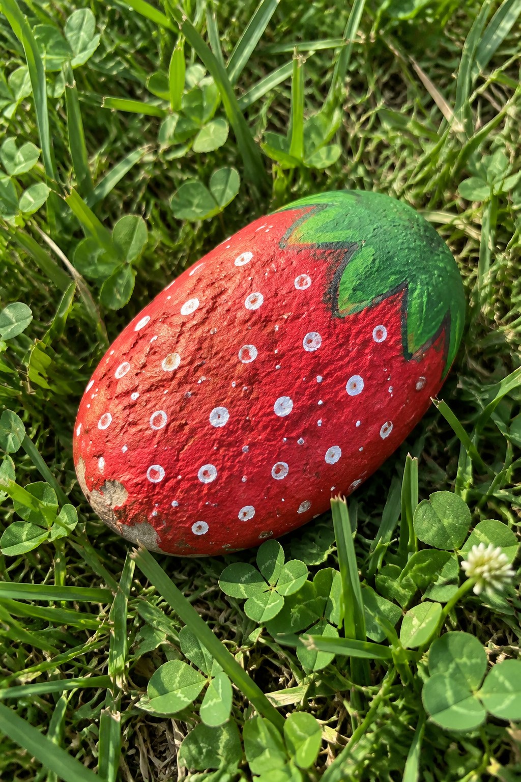 Painted red strawberry rock with white dots and green top on grass