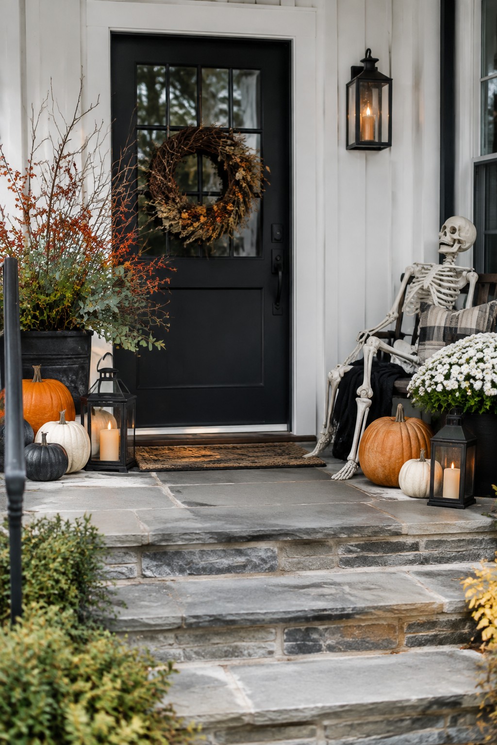 Front porch with a black door and a decorative skeleton seated in a chair next to pumpkins and lanterns.