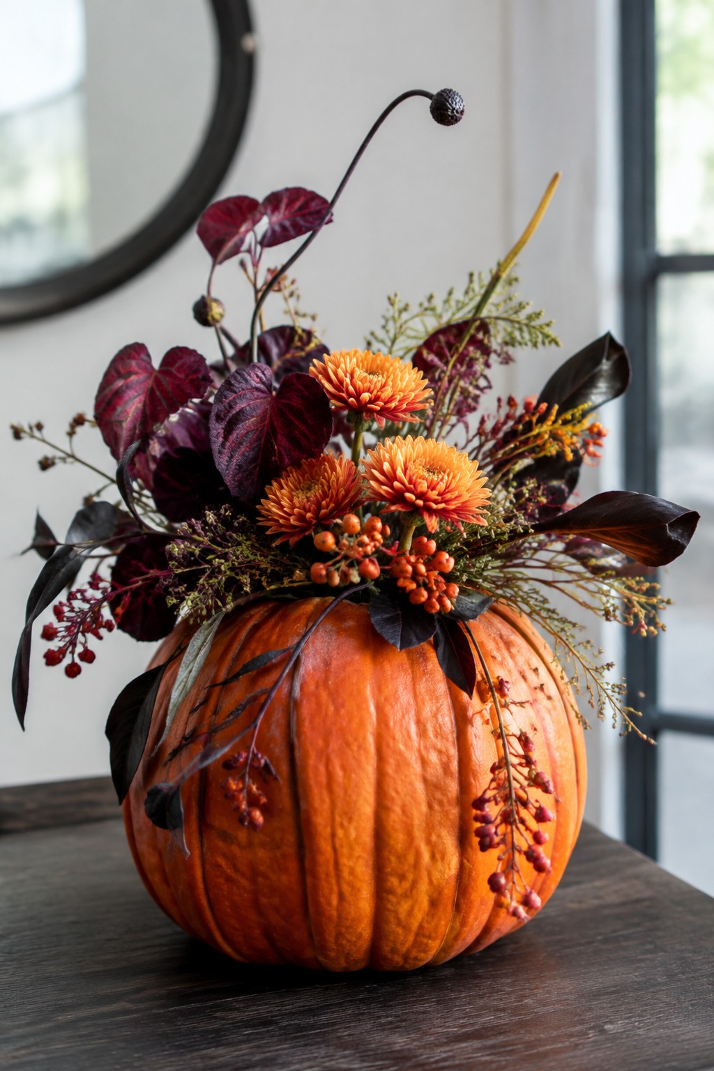 Orange pumpkin vase with orange chrysanthemums, dark purple leaves, and red berries on wood