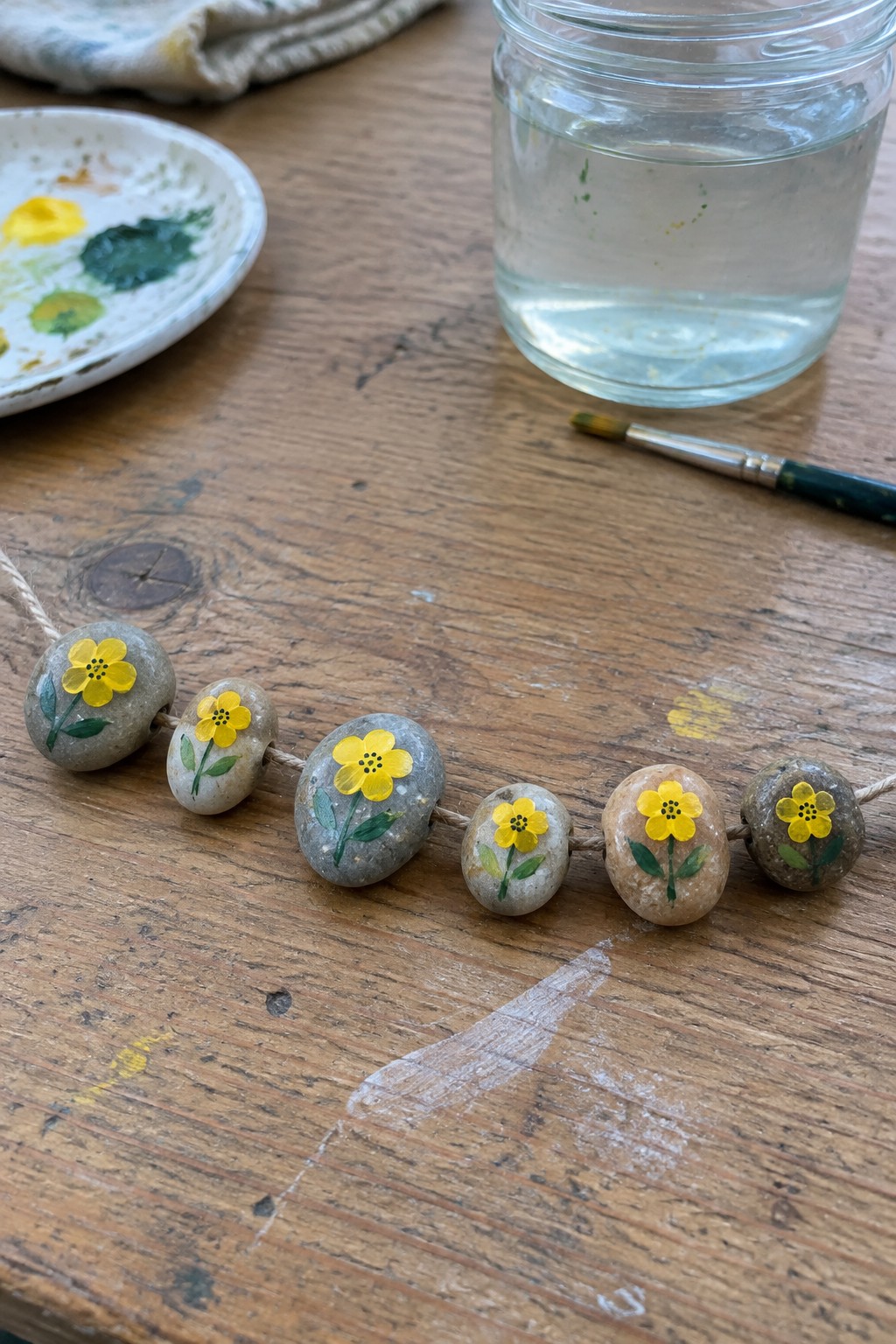 String of gray pebbles painted with yellow flowers on wooden table with paints