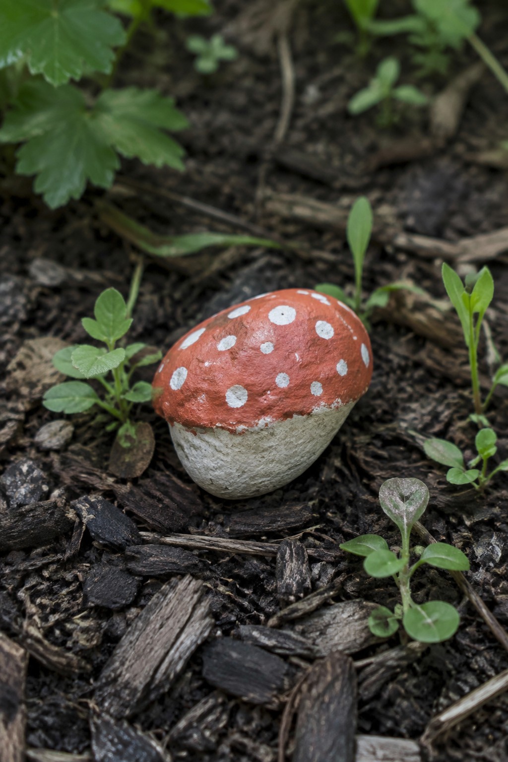 Red mushroom rock with white spots on dark soil amid green plants