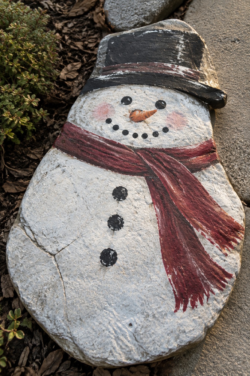 Painted stone snowman with black top hat, red scarf, and coal buttons.